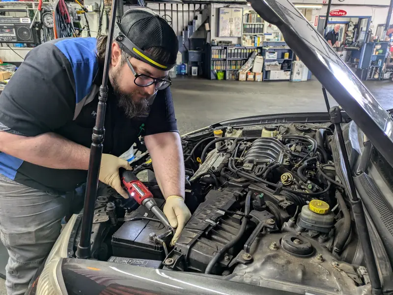 A KC Martin technician tightening a battery terminal under the hood