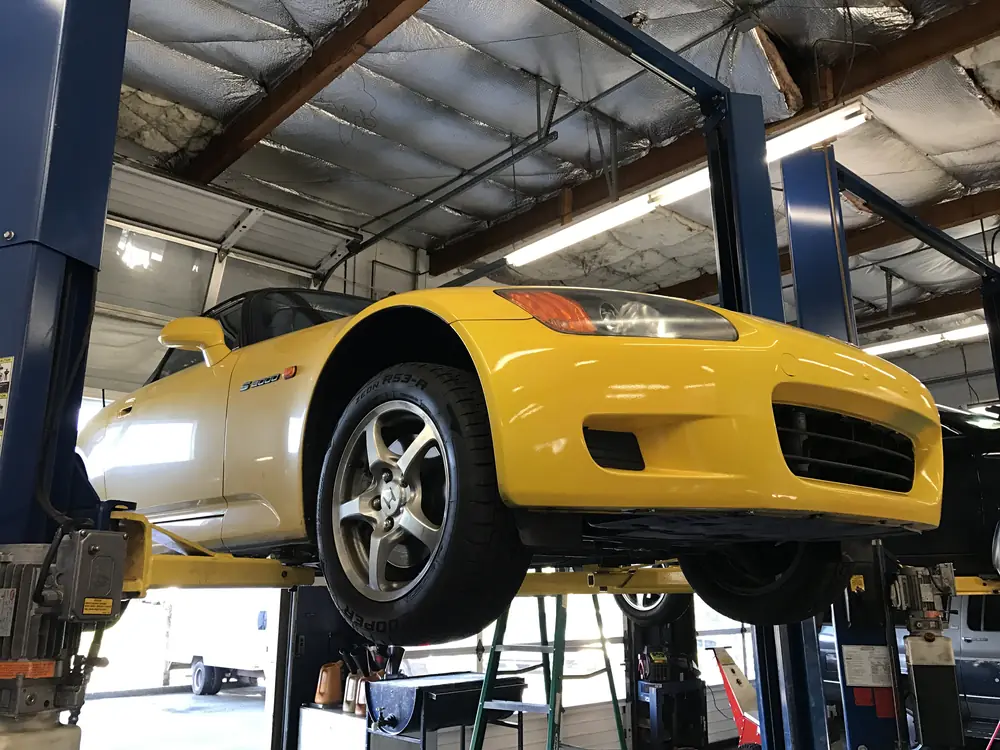 A yellow Honda S2000 raised on a lift