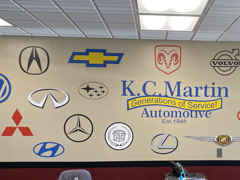The wall of car-maker emblems in the KC Martin front office, with the Subaru emblem beside the shop name