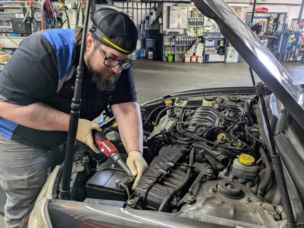 A KC Martin technician working at a car battery with a headlamp on
