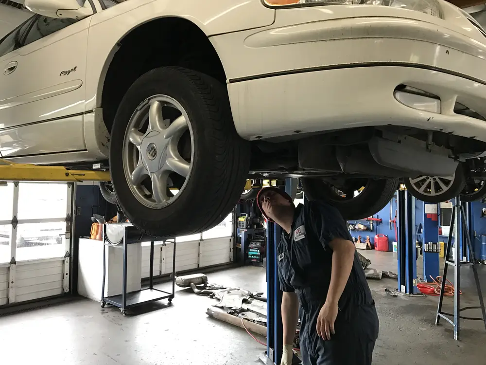 A KC Martin technician under a car on the lift, with the old exhaust pipes on the floor
